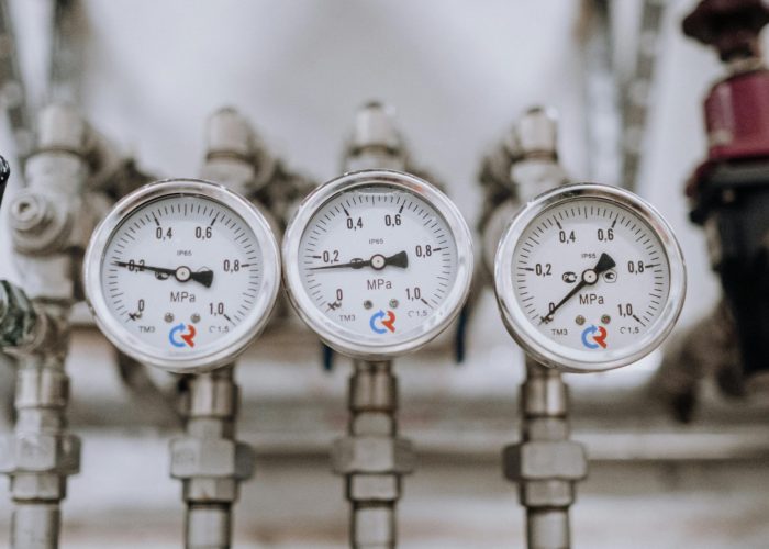 Close-up of three industrial pressure gauges on pipelines indoors.